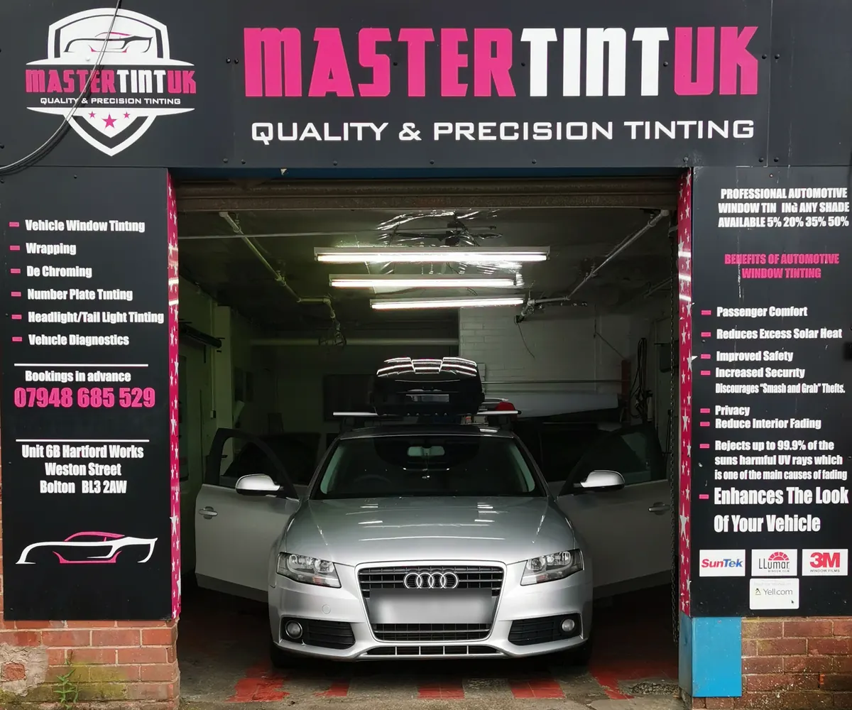 MasterTint UK's open bay: the shield logo and MASTERTINTUK board above, service boards either side and magenta star-print trim on the door frame